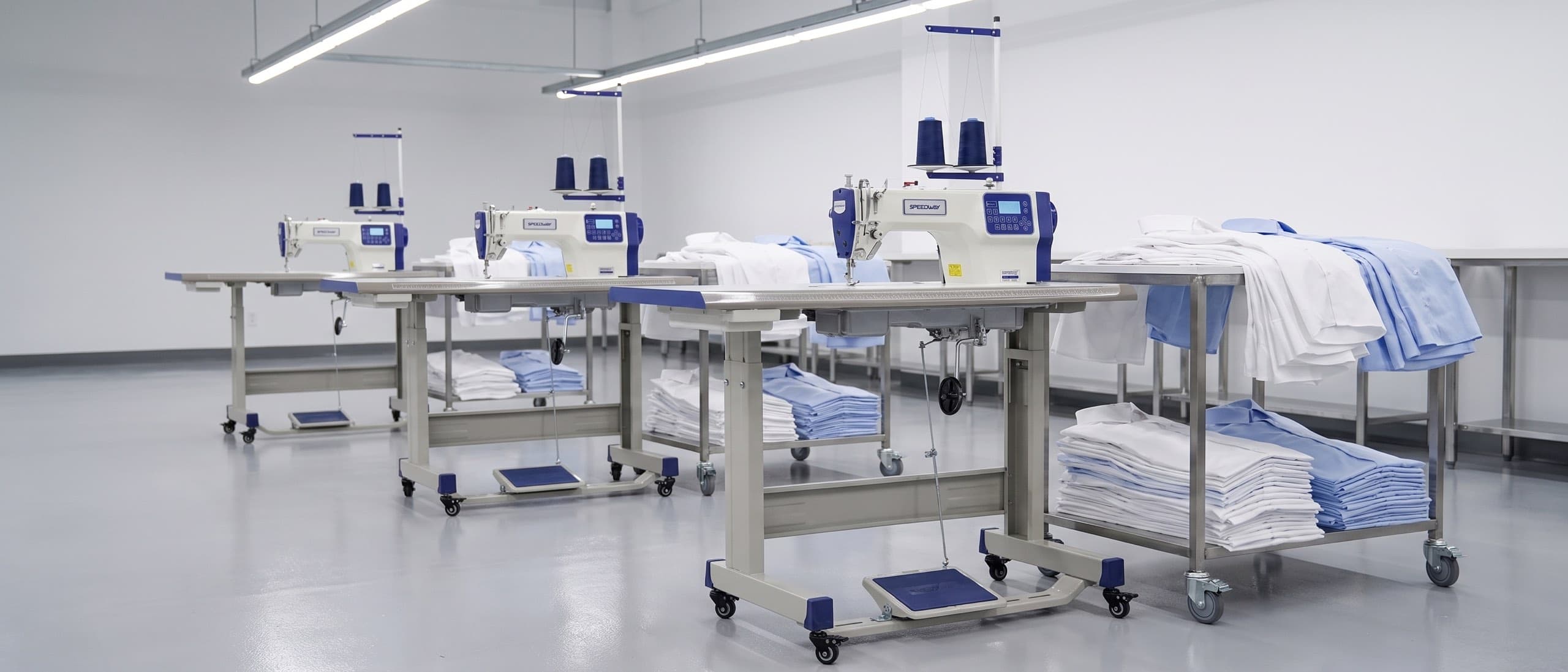 Apparel contract manufacturing line at end of shift — three industrial single-needle lockstitch machines along a long bench, stacks of cut denim panels