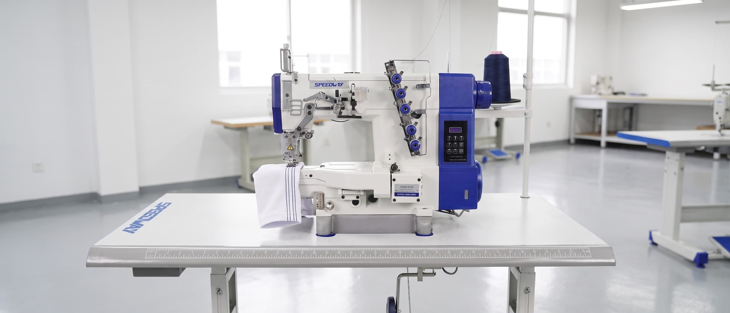 Industrial coverstitch sewing machine laying down three parallel rows on a knit jersey hem, chain stitch loop visible underneath