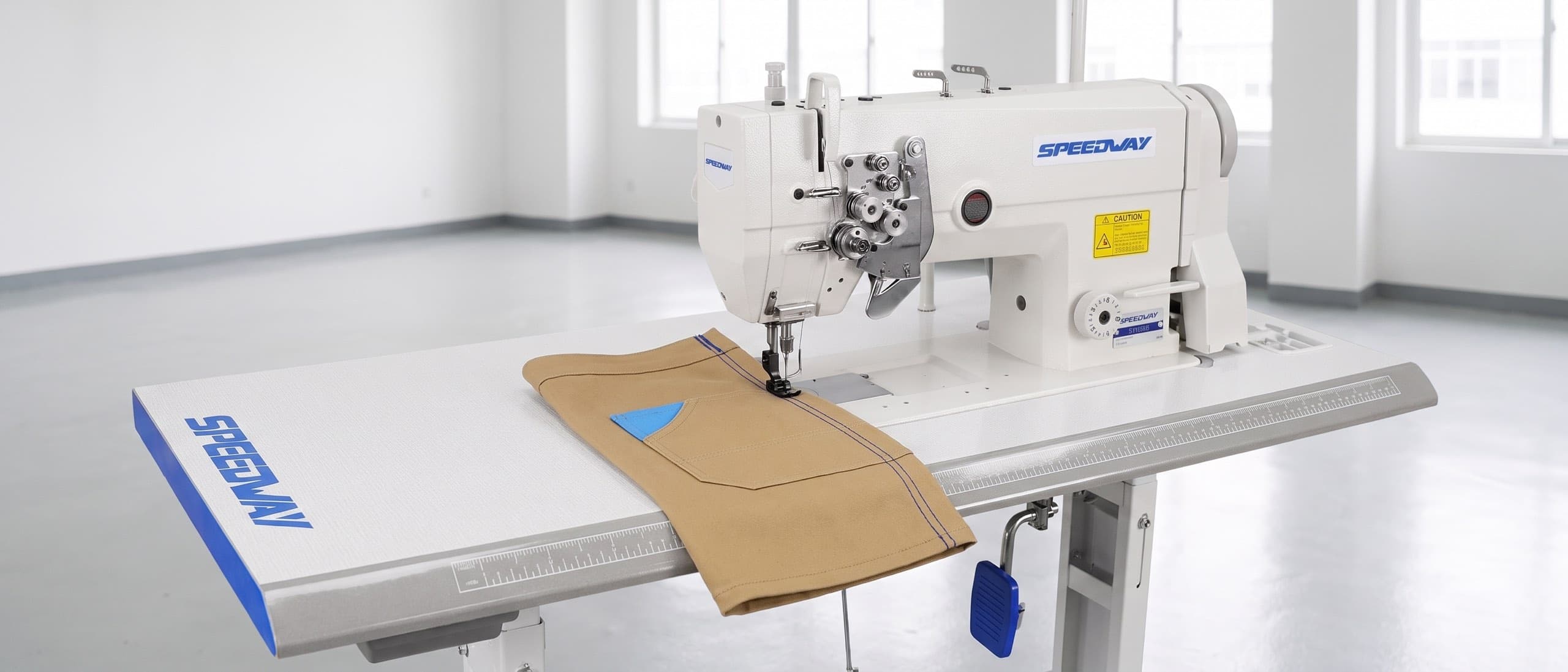 Industrial double-needle lockstitch sewing machine laying down two parallel rows of orange contrasting topstitching on indigo denim