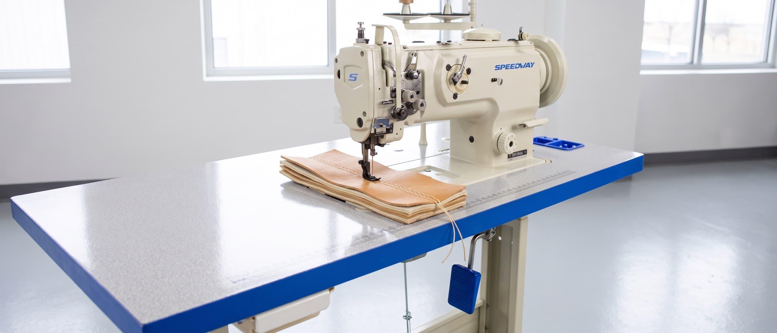 Heavy-duty industrial sewing machine sewing through a six-layer stack of canvas and leather, heavy bonded thread visible